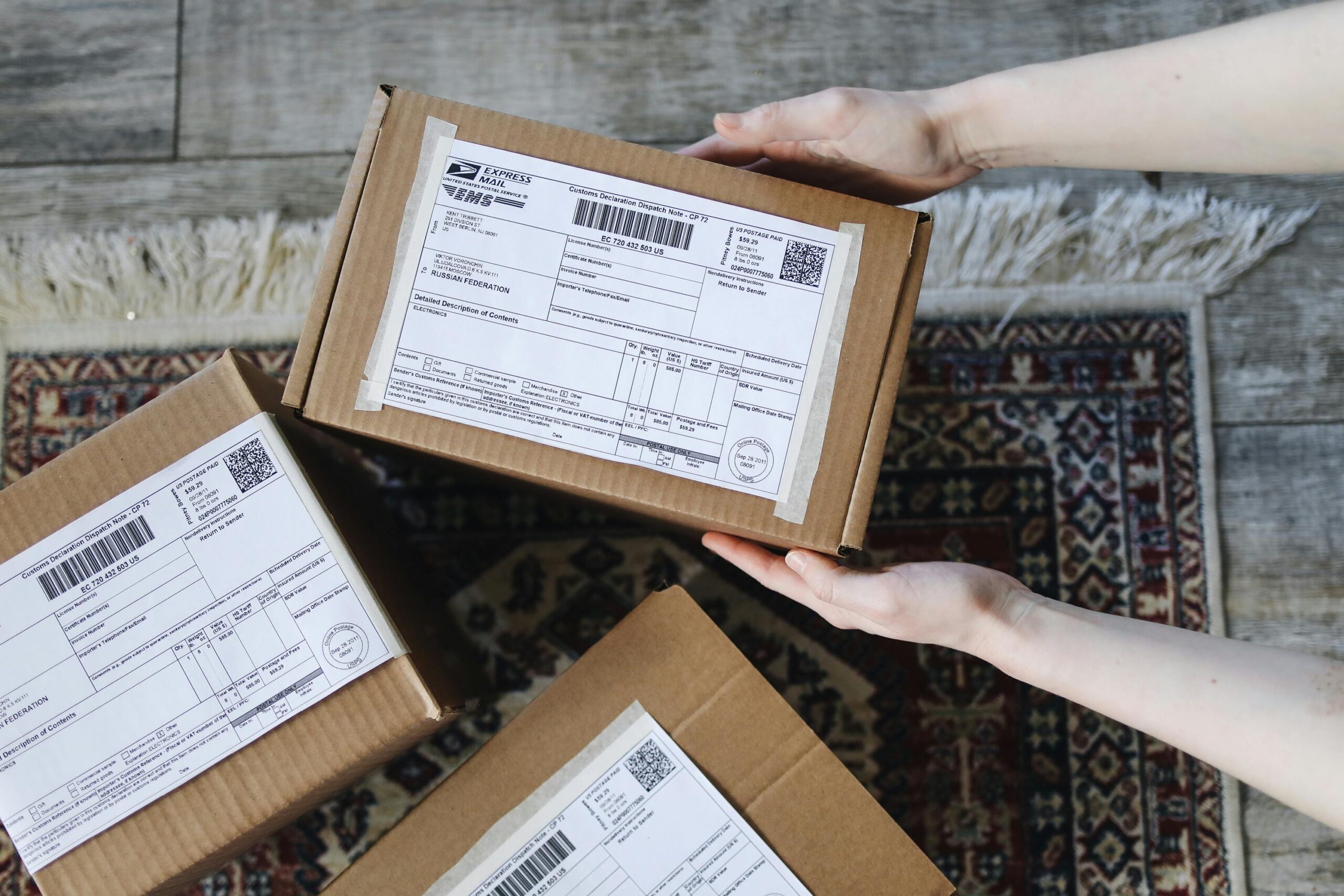 Close-up of hands holding cardboard boxes with labels for delivery on a decorative carpet.